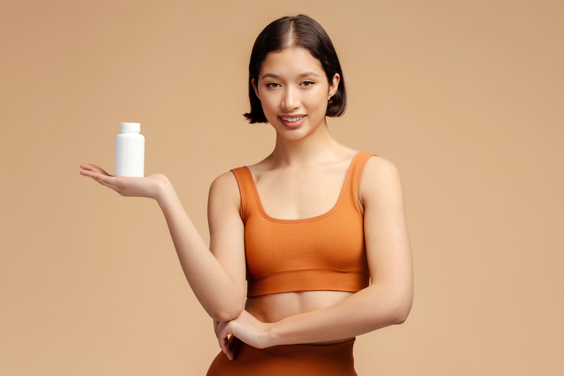 Young athletic fitness woman holding bottle with vitamins and looking at camera isolated